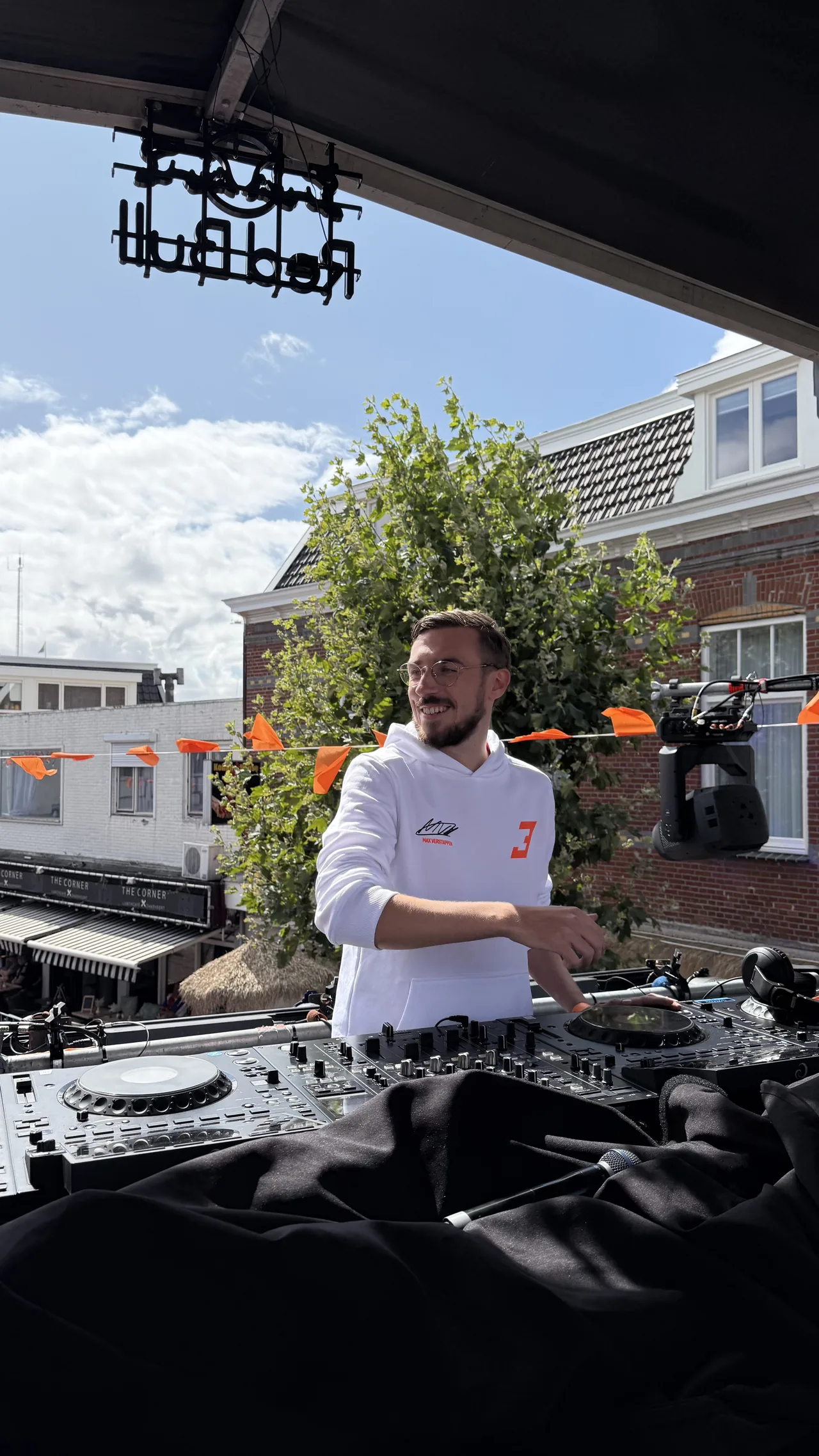 Barry in een witte hoodie bij een buitenoptreden met oranje vlaggetjes